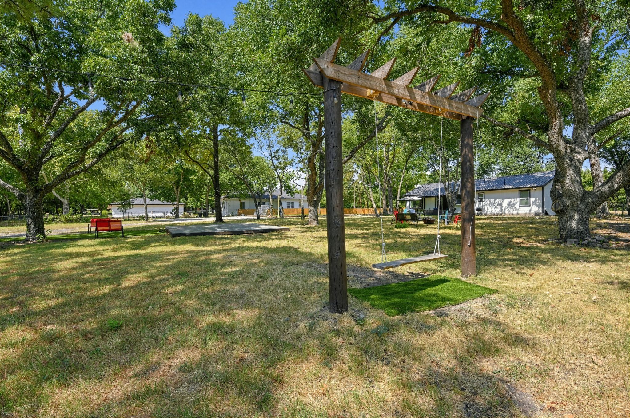 Un parc avec une balançoire en bois, des bancs et une pelouse.