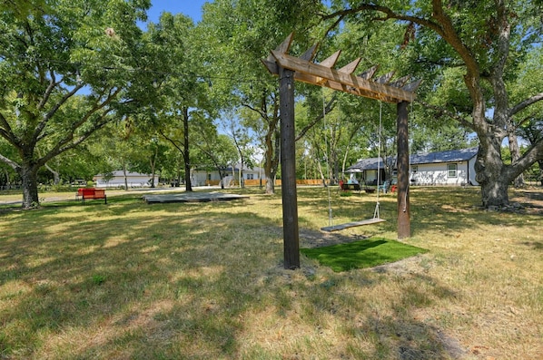 Un parque con un columpio de madera, bancos y una zona verde.