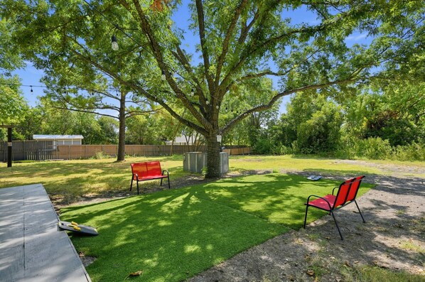 Un patio trasero con un árbol, dos bancos rojos, una mesa de picnic y una valla metálica.