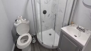 Moderni kylpyhuone, jossa on wc, suihkukaappi ja pesuallas.