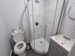 A modern bathroom with a toilet, a shower enclosure, and a sink. - 3BR Family Retreat Mini Golf Soccer Field Fire Pit (Wylie)