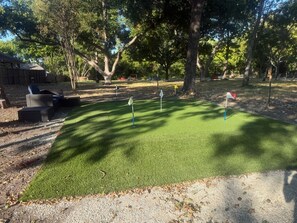 Un campo de golf con un putting green, árboles y una valla de madera.