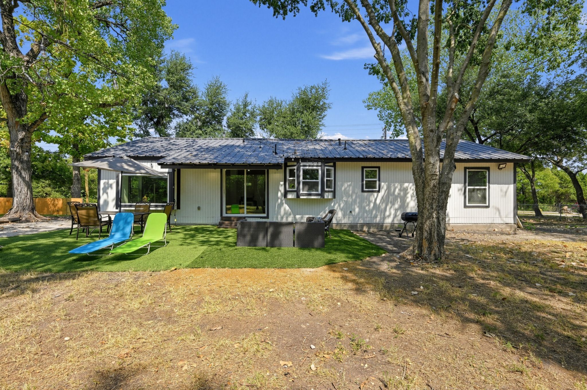 Une maison de plain-pied avec un patio couvert, une pelouse et un ensemble de jeux pour enfants (balançoire, etc.).
