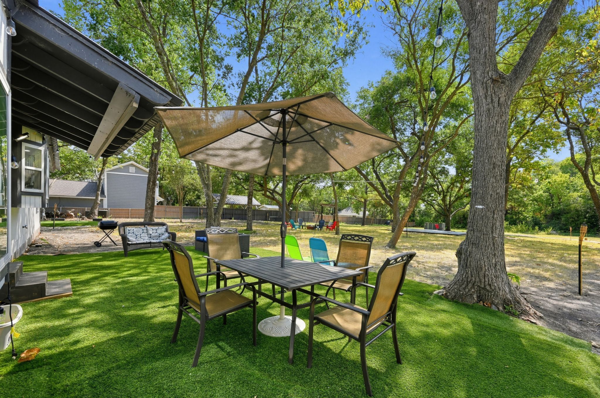 Une terrasse extérieure avec une table et des chaises, entourée d’arbres et d’une pelouse verdoyante.