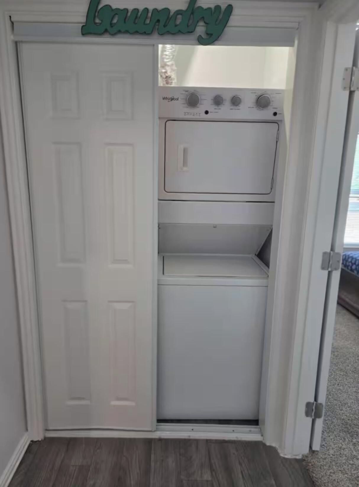A laundry room with a white door, a Whirlpool washer and dryer, and a 'Laundry' sign above the door.