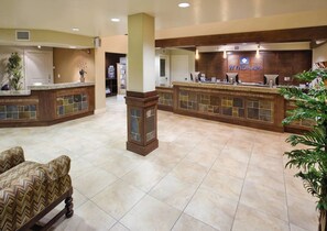Een hotel lobby met een receptiebalie, zithoek en een grote pilaar.