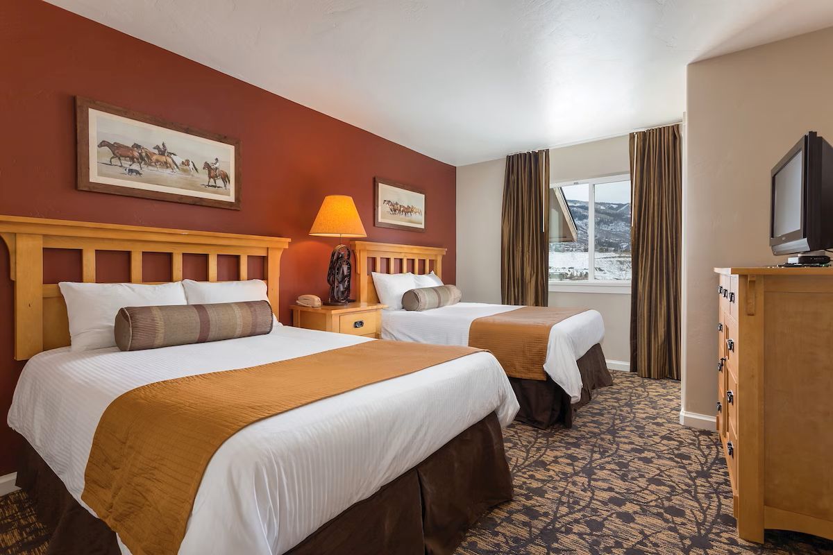 A hotel room with two beds, a television, a dresser, and a window with curtains.