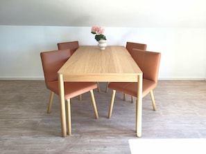 A rectangular dining table with six chairs, a vase with flowers, and a light-colored wooden floor. - Heiligenhafenbude 2 (Heiligenhafen)