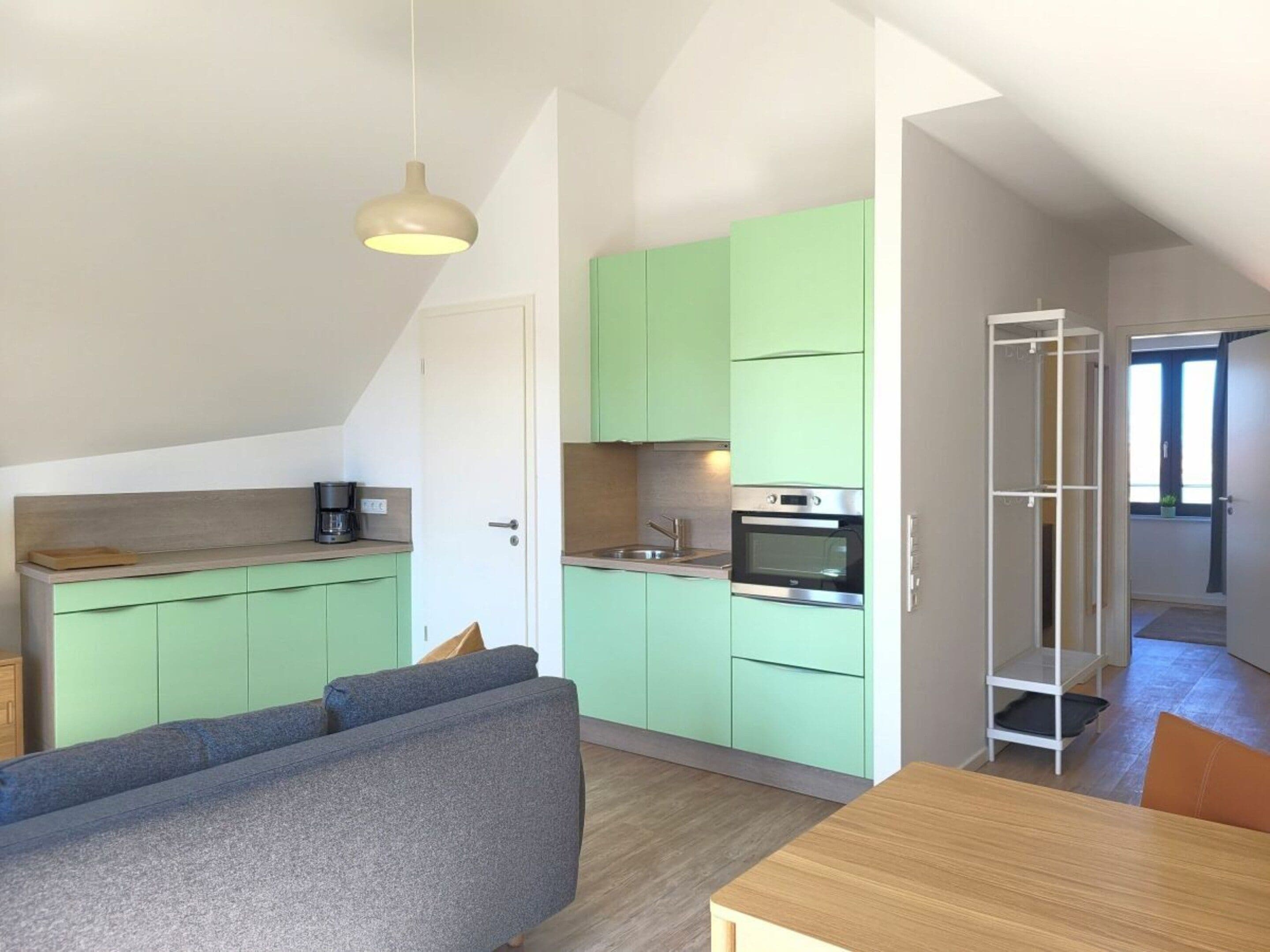 A compact kitchen with green cabinets, a built-in oven, and a coffee maker on the countertop.