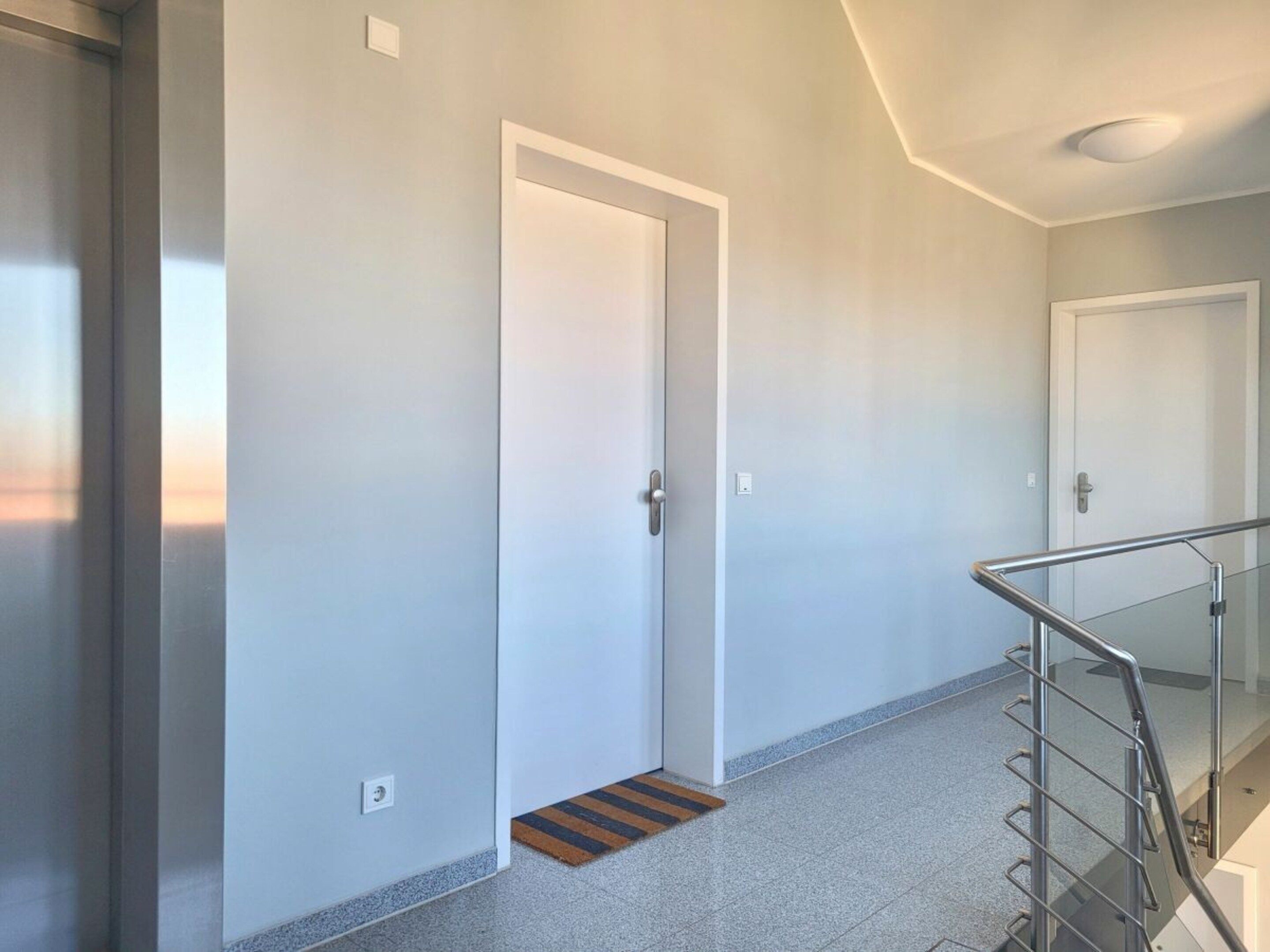 A hallway with a door, a handrail, and a tiled floor.