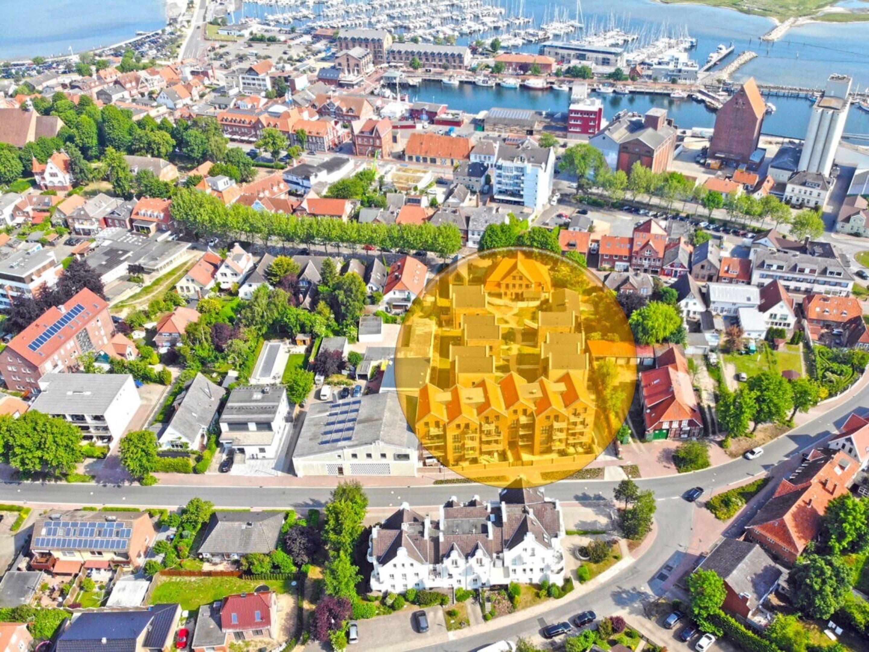 An aerial view of a coastal town with a marina, residential buildings, and a prominent yellow building with a unique geometric design.