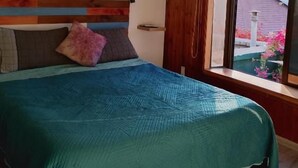 Un dormitori amb un llit, una finestra amb cortines, un quadre a la paret i un aparell d'aire condicionat.