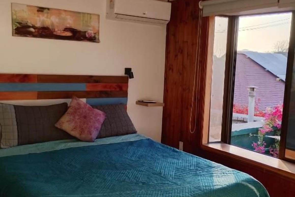 Una camera da letto con un letto, una finestra con tende, un quadro appeso al muro e un condizionatore d'aria.