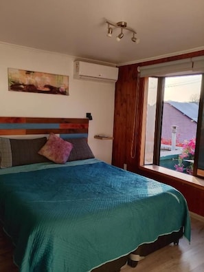 Una camera da letto con un letto, una finestra con tende, un quadro appeso al muro e un condizionatore d'aria.