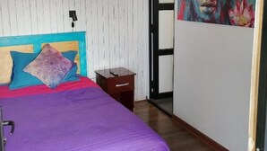 Un dormitori amb un llit, una tauleta de nit, una porta i una paret amb un quadre.