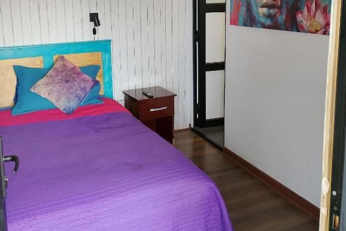 Una camera da letto con un letto, un comodino, una porta e una parete con un quadro.