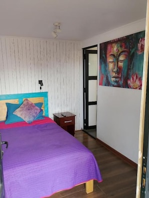 Una camera da letto con un letto, un comodino, una porta e una parete con un quadro.