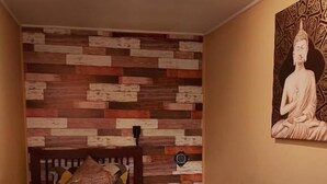 Un dormitori amb llit, panell de capçal de fusta, paret amb disseny decoratiu i una estàtua de Buda.