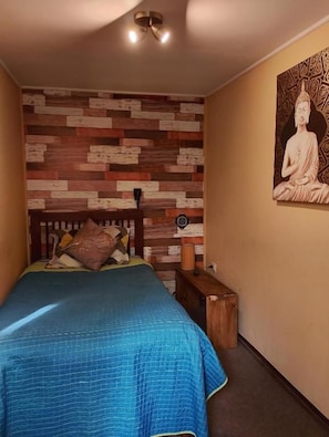 Una camera da letto con un letto, una testiera in legno, una parete con un motivo decorativo e una statua di Buddha.