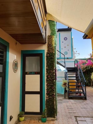Un edificio con una puerta que indica 'BAÑO' y una escalera que sube a un balcón.