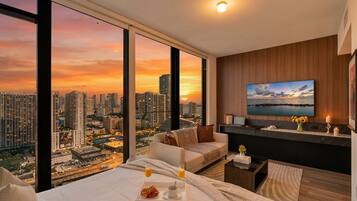 A modern hotel room with a city view, a bed with breakfast, a TV, and a cozy seating area.