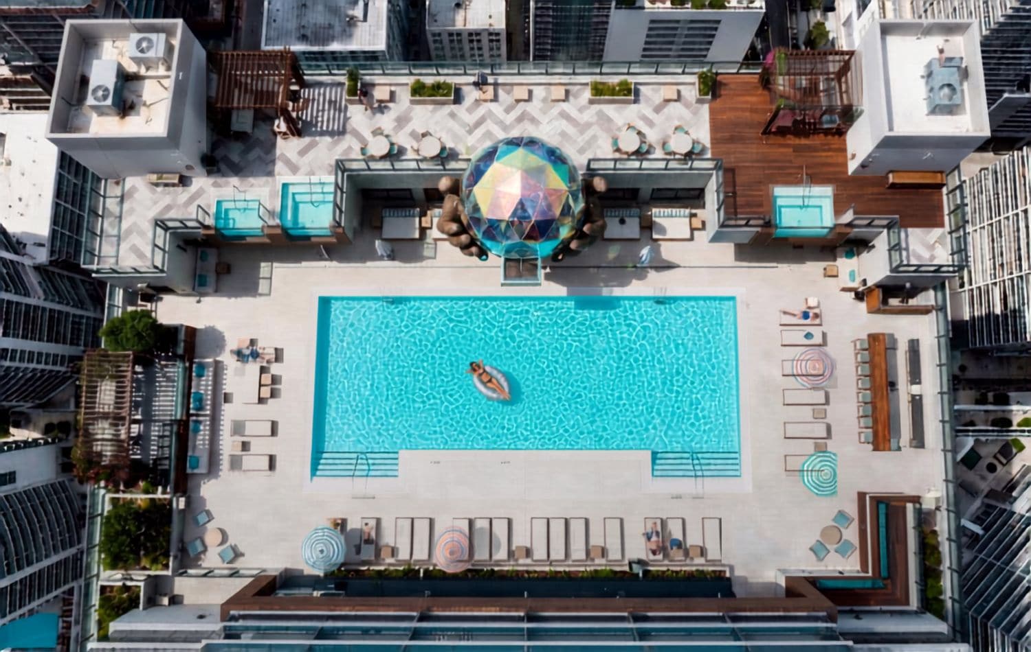 Vista aérea de uma piscina no terraço, com uma escultura esférica central, rodeada por áreas de estar e assentos.