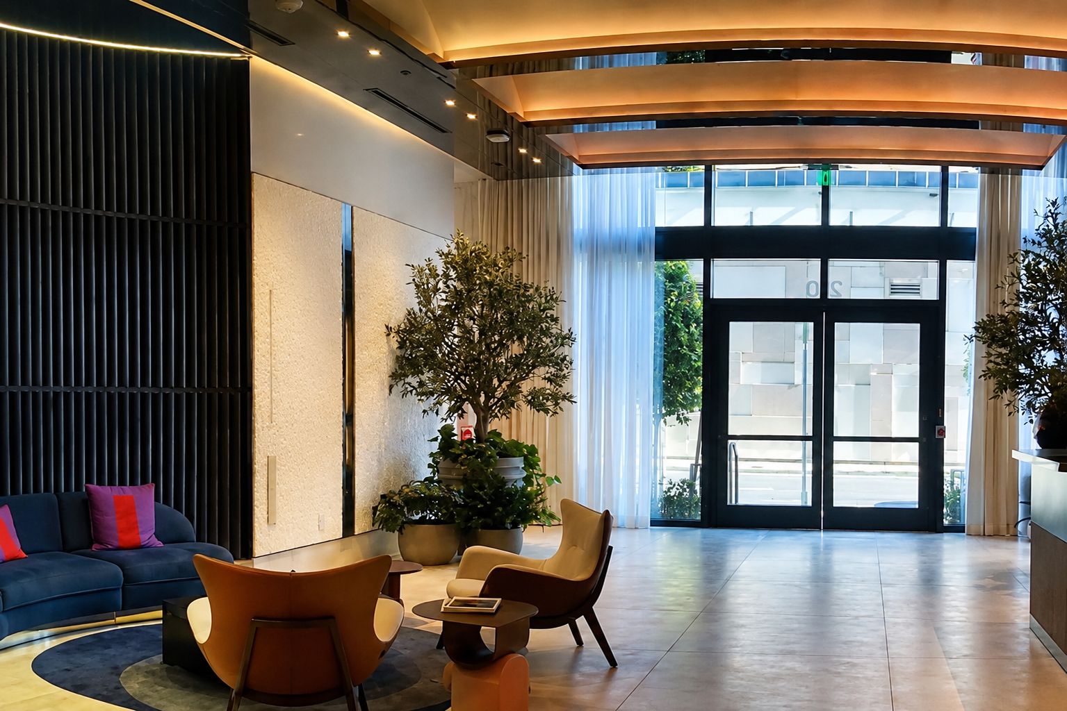 A modern lobby with a curved ceiling, a reception desk, a seating area with chairs and a sofa, and a large window with a view of the outside.