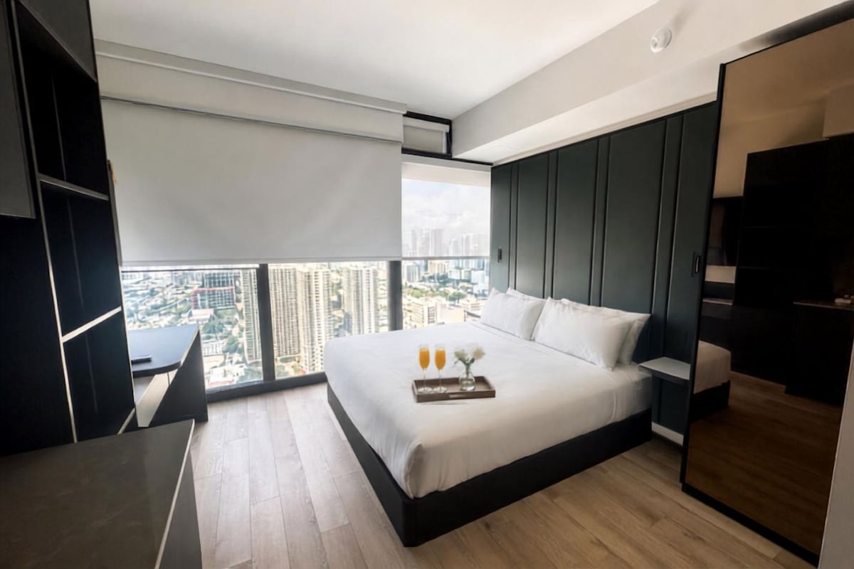 A modern hotel room with a large bed, a desk, and a view of the cityscape.