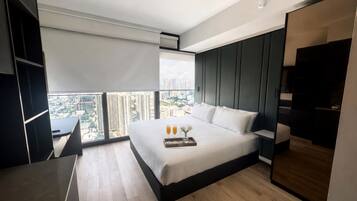 A modern hotel room with a large bed, a desk, and a view of the cityscape.