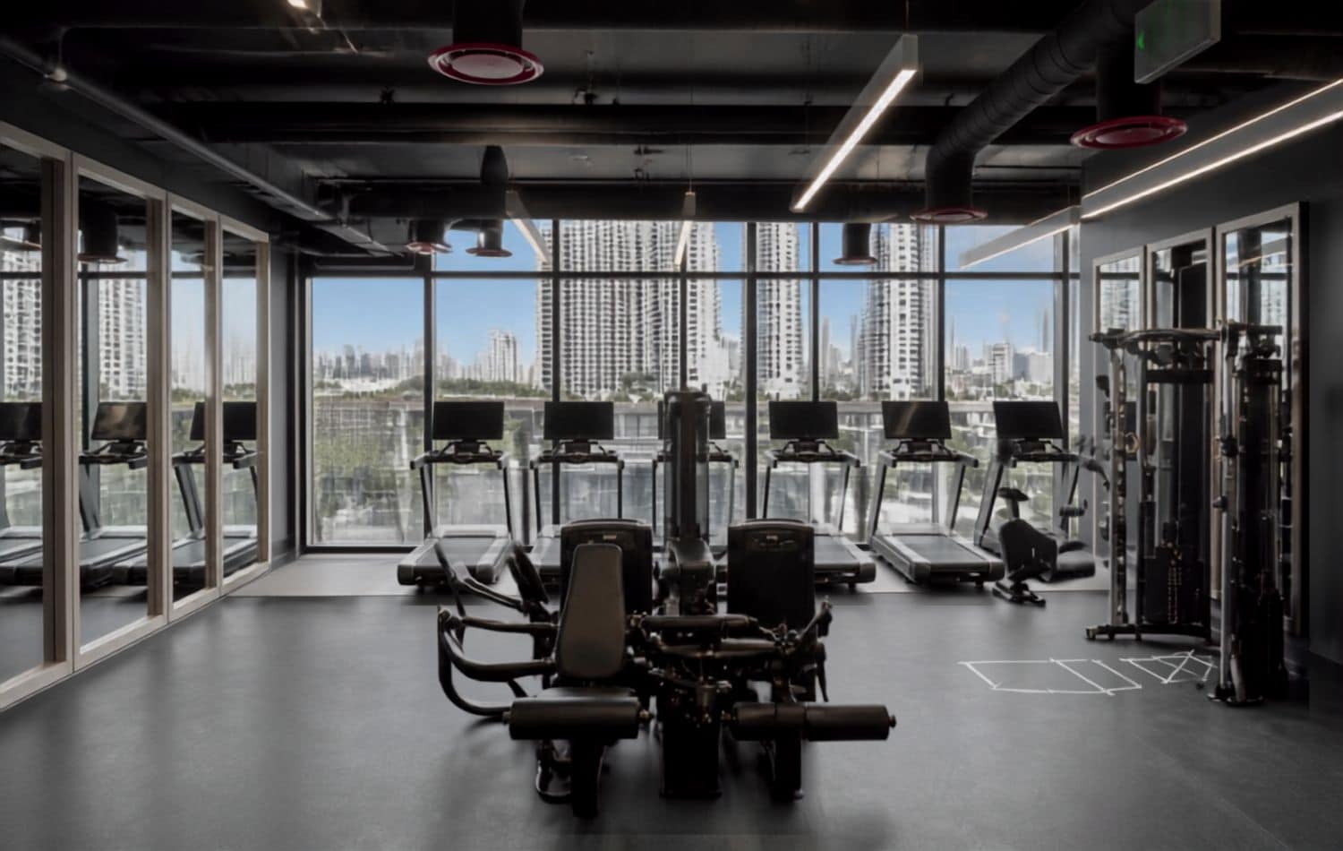 Ein Fitnessstudio mit Laufbändern, Kraftgeräten und Blick auf die Stadt durch große Fenster.