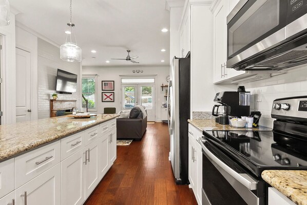 A modern kitchen with white cabinetry, a large island, stainless steel appliances, and a view into the living area.