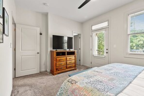 A bedroom with a bed, a dresser, a television, and two doors.