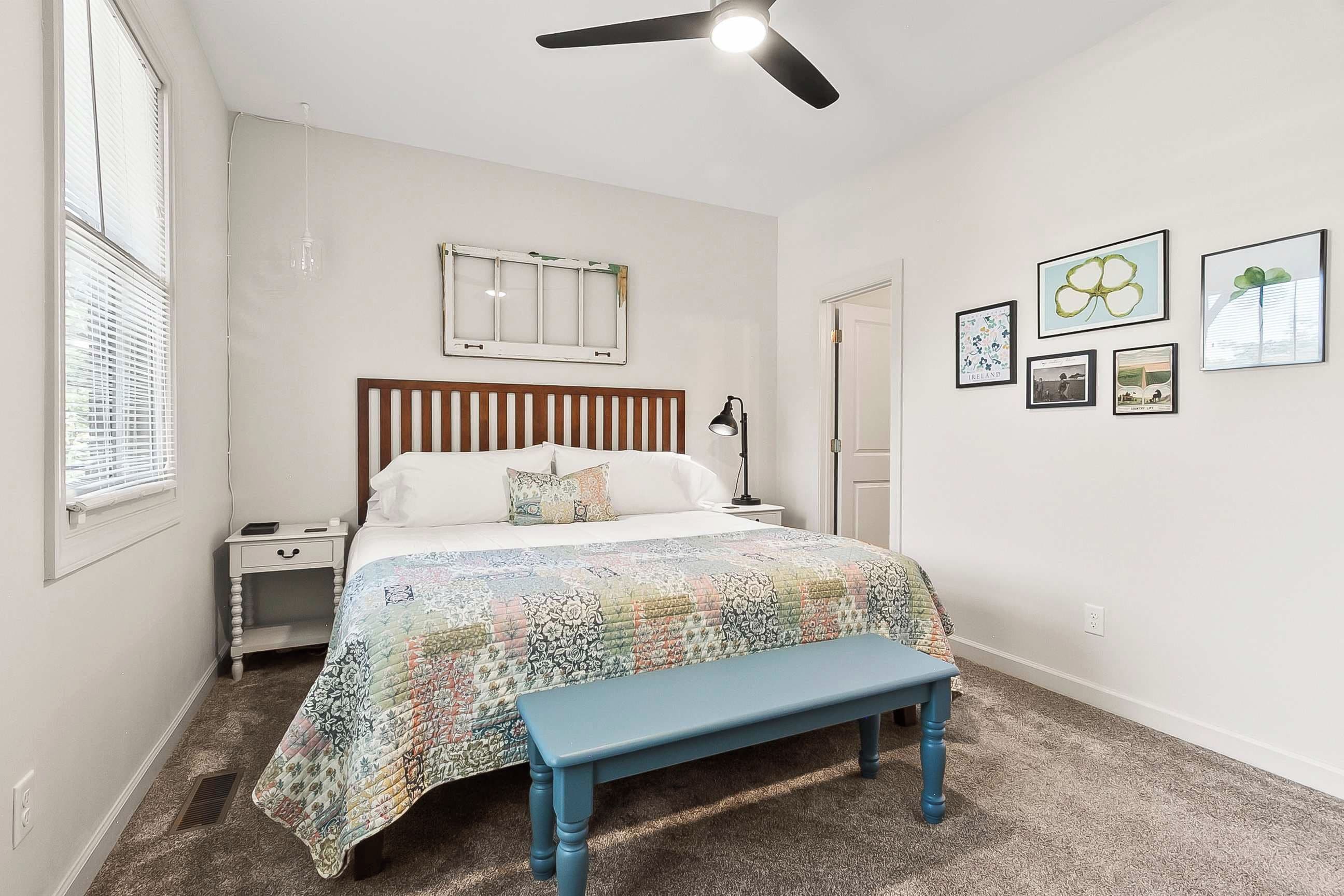 A bedroom with a bed, a nightstand, a bench, a ceiling fan, and wall art.