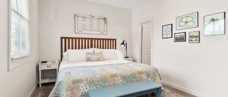 A bedroom with a bed, a nightstand, a bench, a ceiling fan, and wall art.
