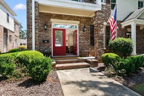 A two-story house with a red door, a brick exterior, and an American flag.