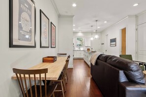 Een moderne keuken met witte kasten, een houten eettafel met stoelen en een bruine leren bank.