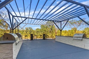 An outdoor patio with a metal roof structure, stone walls, and built-in barbecue grills.