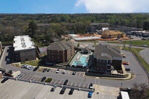 A parking lot with multiple rows of cars, a swimming pool, and several buildings with different architectural styles.
