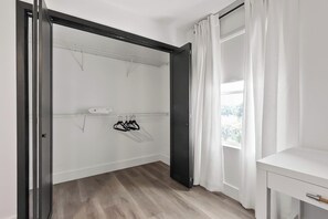 A room with a wooden floor, a white wardrobe, a black door, and a window with white curtains.