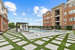 A swimming pool with lounge chairs, a pergola, and a brick building with balconies.