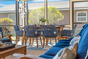 A sunlit patio area with wicker furniture, a table, and a view of a building and trees. - Casa Coco (Cocoa Beach)