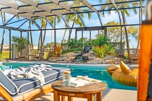 Uma área de piscina com espreguiçadeiras, uma pequena mesa com uma bebida e vista para o exterior.