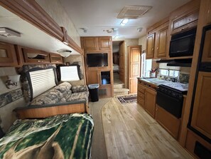 A compact RV interior with a kitchenette, a seating area, and a television.