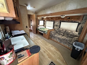 A compact RV interior with a kitchenette, a bed, and a seating area.