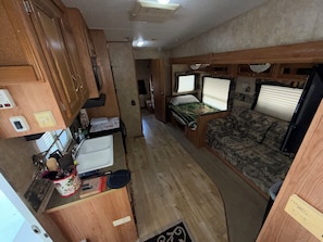 A compact RV interior with a kitchenette, a bed, and a seating area.
