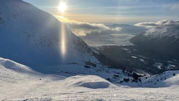 A snow-covered mountain landscape with a clear sky and the sun shining from behind the peaks.