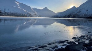 Ein gefrorener See mit Bergen im Hintergrund und der Sonne, die sich auf der Wasseroberfläche spiegelt.