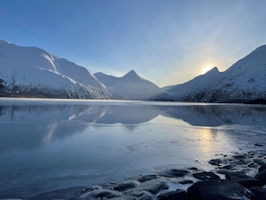 Un lago helado con montañas al fondo y el sol reflejándose en el agua.