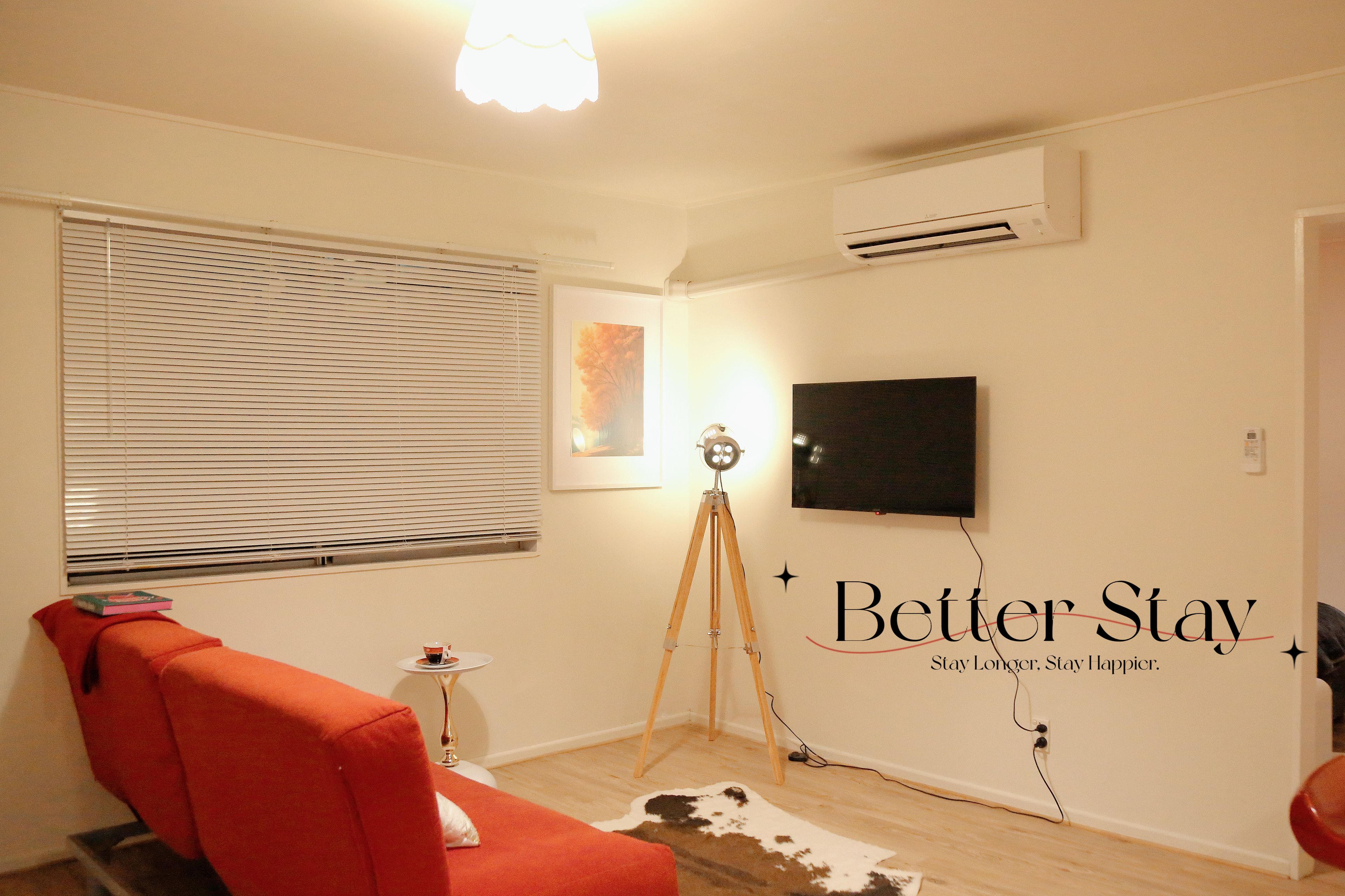 A room with a red sofa, a tripod, a mounted television, and a wall-mounted air conditioner.