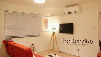 A room with a red sofa, a tripod, a mounted television, and a wall-mounted air conditioner.